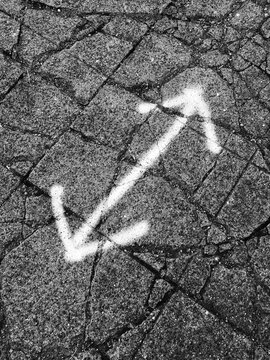 Spray painted double arrow sign on worn and cracked sidewalk