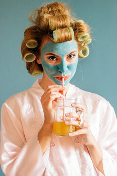 Portrait of a young female model with facial mask and curlers at her home