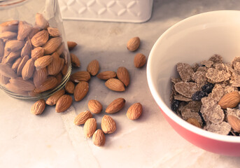 Disfruta de un saludable y delicioso desayuno acompañado con frescas almendras y un bowl de cereales vistos desde un ángulo levemente elevado y sobre una encimera de mármol gris. 
