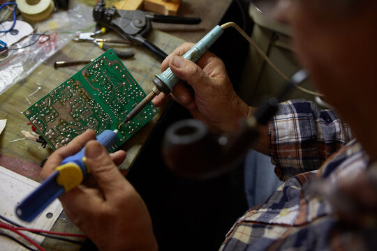 Senior Male Working on Circuit Board while Smoking a Pipe