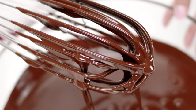 Close up sweet delicious dark melted chocolate on whisk that spins in slow motion. Making premium hand-crafted chocolate. Preparing pralines, candy or truffles concept, pastry, bakery, patisserie
