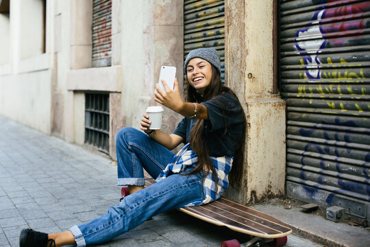 Skater girl taking a selfie sitting on her longboard.