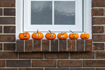 Pumpkins with emoticon faces lined up on a window sill