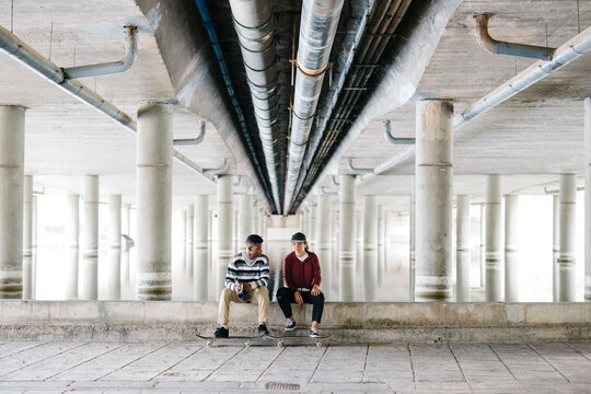 Couple of friends sitting with skateboards.