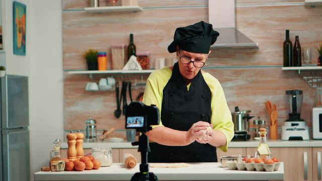 Grandmother making cooking vlog, recording herself on camera. Retired blogger chef influencer using internet technology communicating, shooting blogging on social media with digital equipment