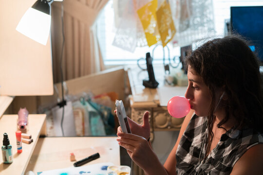 Teenager blowing a chewing gum bubble while using her mobile phone at the desk