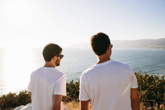Two young man friends looking at the sea at sunset from a hill.