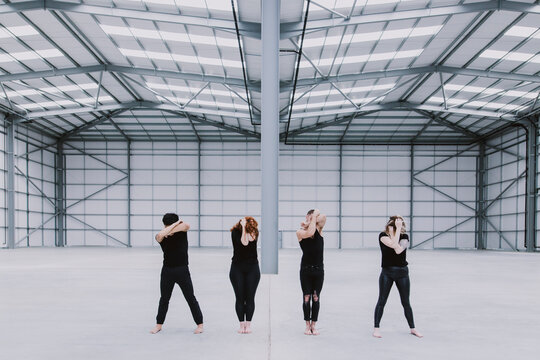 Four dancers standing in a row with their hands over their faces