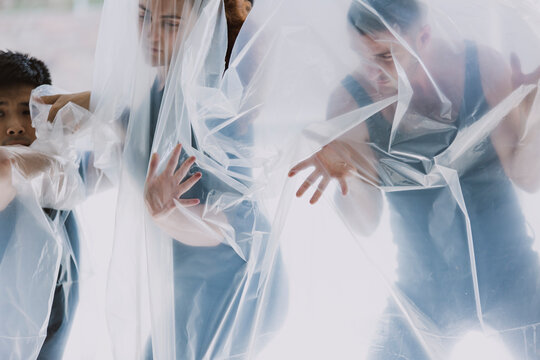 Three people appear to be stuck behind a sheet of plastic, they are pressing forward as though trying to get through