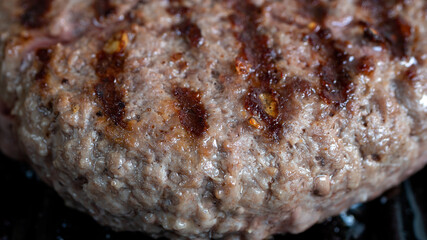 Hamburger patty getting cooked in a cast iron grill pan. Charred burn marks from the pan are clearly visible.
Hamburger meat and food preparation concept.