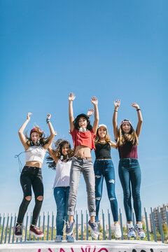 Group of five teens jumping against a blue sky