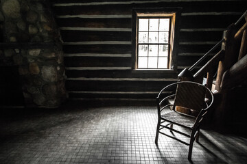 Empty Room With Single Chair. Sunlight streams through the window of a cabin with an empty wooden...