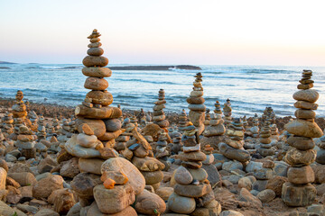 Beach with several balanced stone towers built by people at sunset