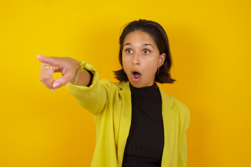 Young hispanic businesswoman wearing casual turtleneck sweater and jacket Pointing with finger surprised ahead, open mouth amazed expression, something on the front.