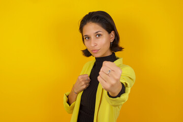 Young hispanic businesswoman wearing casual turtleneck sweater and jacket Punching fist to fight, aggressive and angry attack, threat and violence