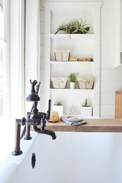Close-up of clawfoot bathtub with bath products on wood caddy in small rustic farmhouse cottage