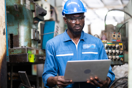 Male Engineer Working On Laptop Computer In Factory. Black Male Engineer Checking Quality Control The Condition Of The Machine. Service And Maintenance Of Factory Machinery