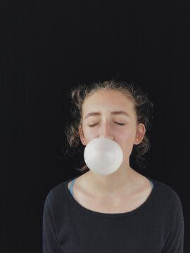 Teenage girl concentrating and blowing bubble gum bubble