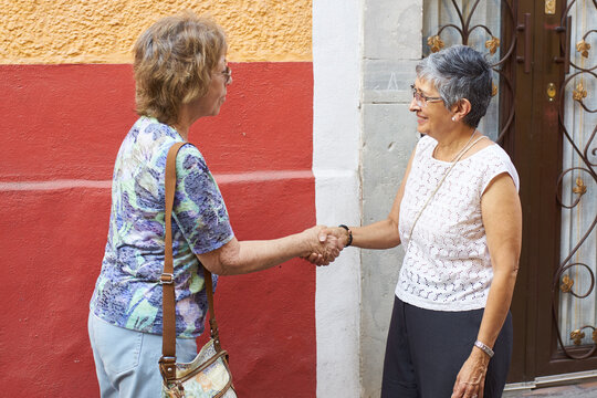 Two women shake hands outside house