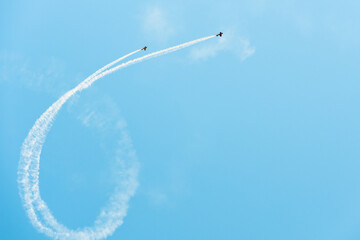 Planes doing aerial acrobatics and dropping smoke in a curved shape on a clear blue sky with copy space.