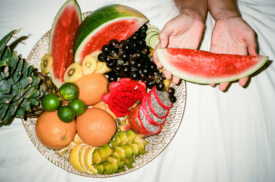female legs crossed on bed eating fruit from giant tray compilation of colorful fruits