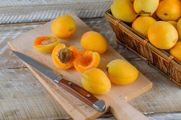 Apricots with knife in a basket on wooden and cutting board background, high angle view.