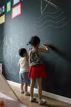 Adorable brother and sister drawing on blackboard wall