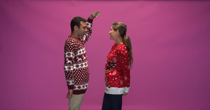 Studio, slow motion, young man surprises his female friend with a small mistletoe