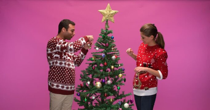 Studio shot of a woman and a man decorating a christmas tree, slow motion