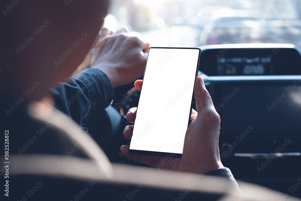 Poster mock up of man using and looking at blank screen mobile phone inside a car on the road