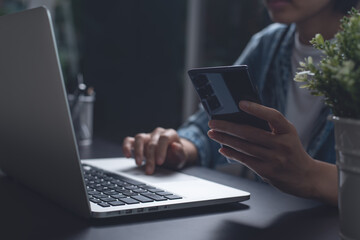 Woman using mobile phone while overtime working on laptop computer at night from home office