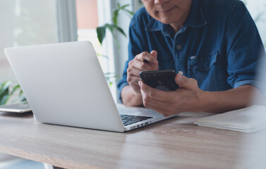 Casual business man video calling on mobile smart phone while working on laptop computer