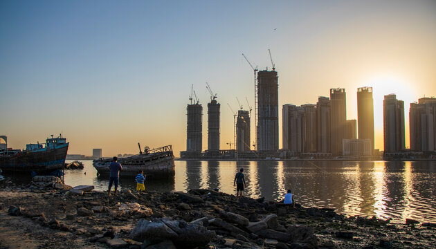 Sunrise in Jadaf area of Dubai, view of Dubai creek Harbor construction of which is partially completed. Old abandoned ships can be seen on the scene. Some men fishing.