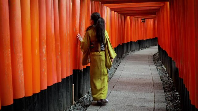 Elegant Japanese woman walking along a path lined with Torii Gates.