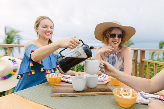 Female Friends Sitting at Breakfast Table on Balcony Sharing Coffee from French Press