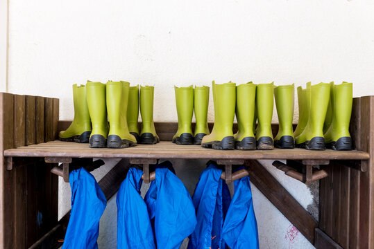 A row of bright green rain boats hang above a bench with matching rain boots below.
