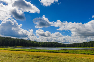Obraz premium Stunning landscape with a lake, field, haystacks and gorgeous clouds in the sky