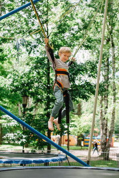 Side view of happy blond boy jumping on trampoline bungy