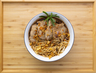 Thai Style Spicy Pork Noodles (Tom Yam) made from Chinese vermicelli with boiled minced pork, deep-fried garlic, and rosemary, serve in a bowl that place on a bamboo wood tray background.