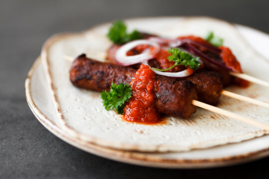 Cevapcici on wooden skewers with onions, parsley and ajvar.
