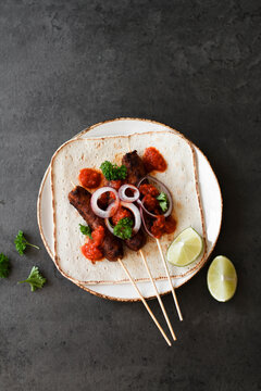 Cevapcici on wooden skewers with onions, parsley and ajvar.