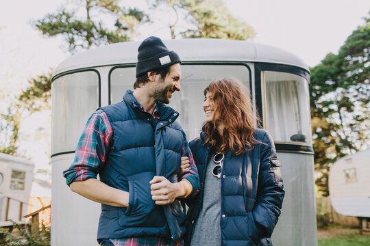 Cute Couple Laughing In Front Of Airstream Trailer