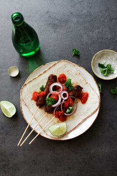 Cevapcici on wooden skewers with onions, parsley and ajvar.