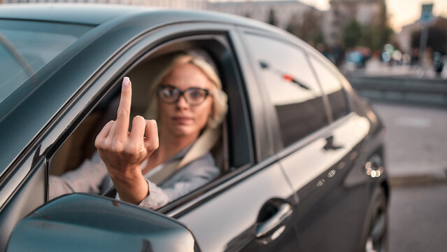 Angry businesswoman. Portrait of aggressive woman in classic wear showing middle finger to somebody while driving a ca