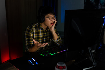 Fototapeta na wymiar Asian man gamer in headphones stressed with hand feel depressed or angry shocked when losing the video game on computer Fear and upset for mistake, video game technology and e-sport concept