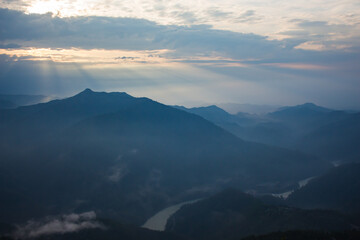 Obraz na płótnie Canvas beautiful landscape of hills silhouette during sunrise. light breaking through cloud cover.