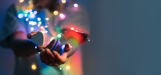 Love symbol. Support compassion. Festive decoration. Heart in caring female hands with Christmas bokeh lights in blur rainbow color gradient glow isolated on navy blue copy space background.