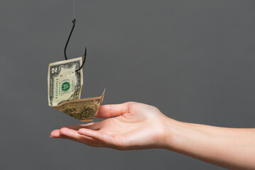 Human hand is holding a dollar on the fishing hook close up on gray background.