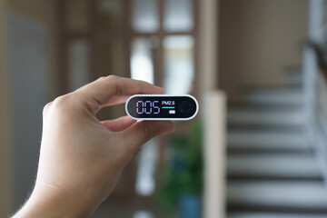 Hand holding portable air quality detector (pm 2.5)  with indoor background.