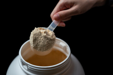 Woman's hands holding measuring scoop of whey protein powder over jar.